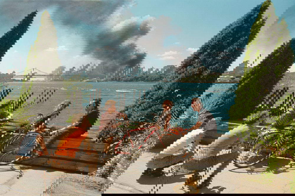 Thomas Hoepker, Young people relax during their lunch break along the East River while a huge plume of smoke rises from Lower Manhattan after the attack on the World Trade Center, New York City, September 11, 2001 - Young people relax during their lunch break along the East River while a huge plume of smoke rises from Lower Manhattan after the attack on the World Trade Center (September 11, 2001; New York City) &copy; Thomas Hoepker/Magnum Photos