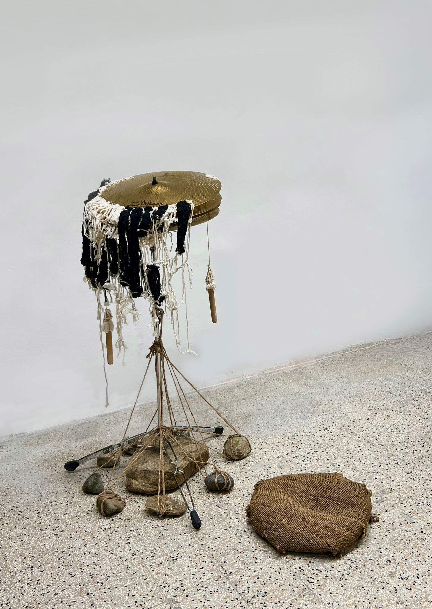 Yiwen Zheng, Time of the Moment (2023; cuerda de algodón, cuerda de cáñamo, platillos ride, trípode, cojín, piedra, 135 x 60 x 60 cm)