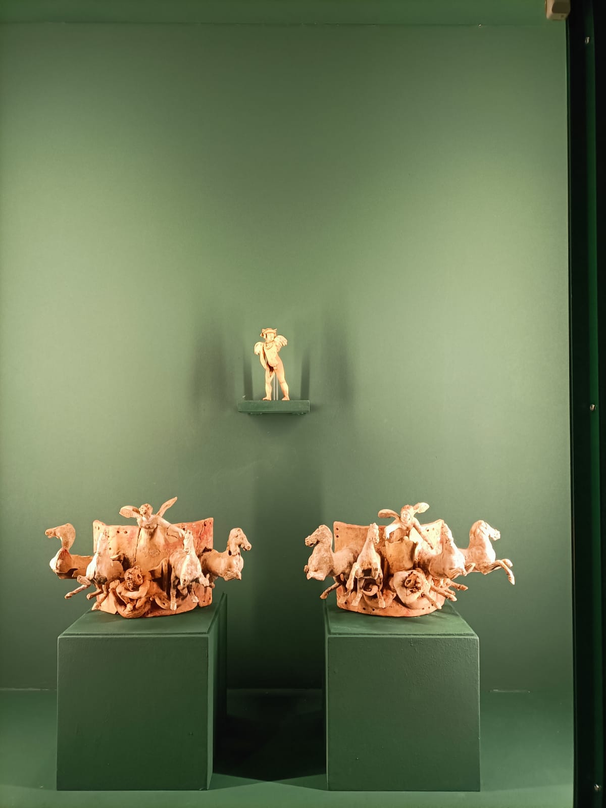 Zwei Applikationen, die eine Quadriga darstellen, die von einer geflügelten Nike angeführt wird (erste Jahrzehnte des 3. Jahrhunderts v. Chr.) und eine Applikation, die einen mit Efeublättern gekrönten Eros darstellt.