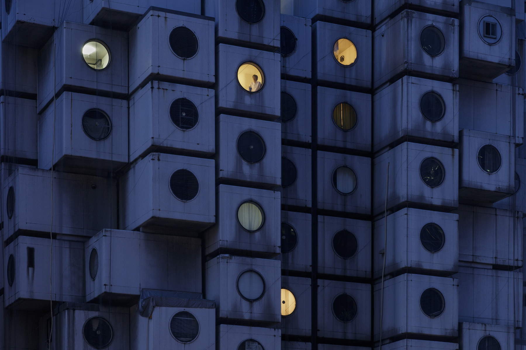 Nakagin Capsule Tower di notte, con Takayuki Sekine visto attraverso la finestra della capsula B1004 (2016) &copy; Jeremie Souteyrat