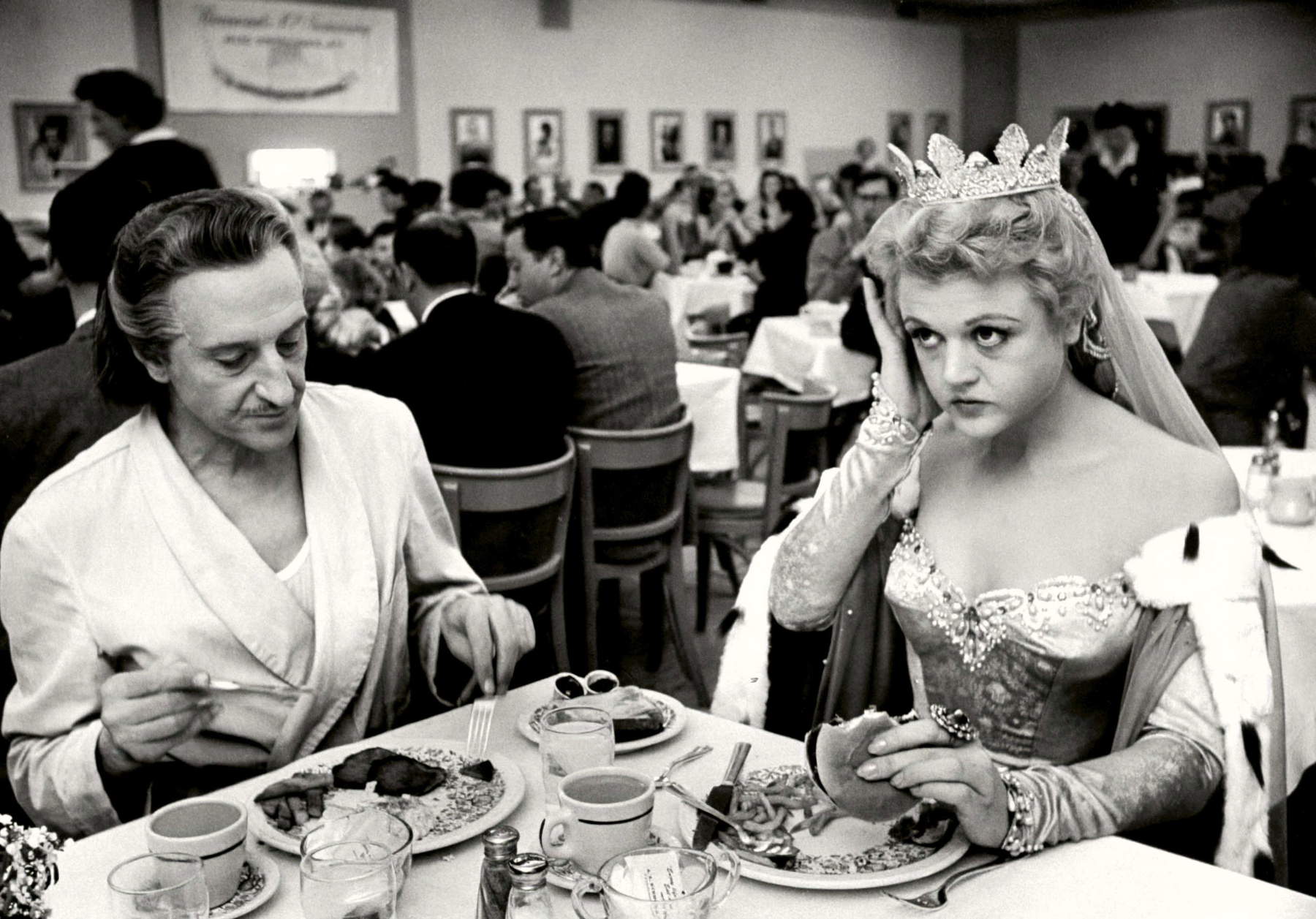 Alfred Eisenstaedt: Die Schauspielerin Angela Lansbury, im Kostüm für den Film „Der Hofnarr&ldquo;, isst an einem Drehtag zusammen mit dem Schauspieler Basil Rathbone im großen Kantinenbereich der Paramount Studios zu Mittag einen Hamburger (Hollywood, Kalifornien, 13. Dezember 1954) &copy; Alfred Eisenstaedt / The LIFE Picture Collection / Shutterstock
