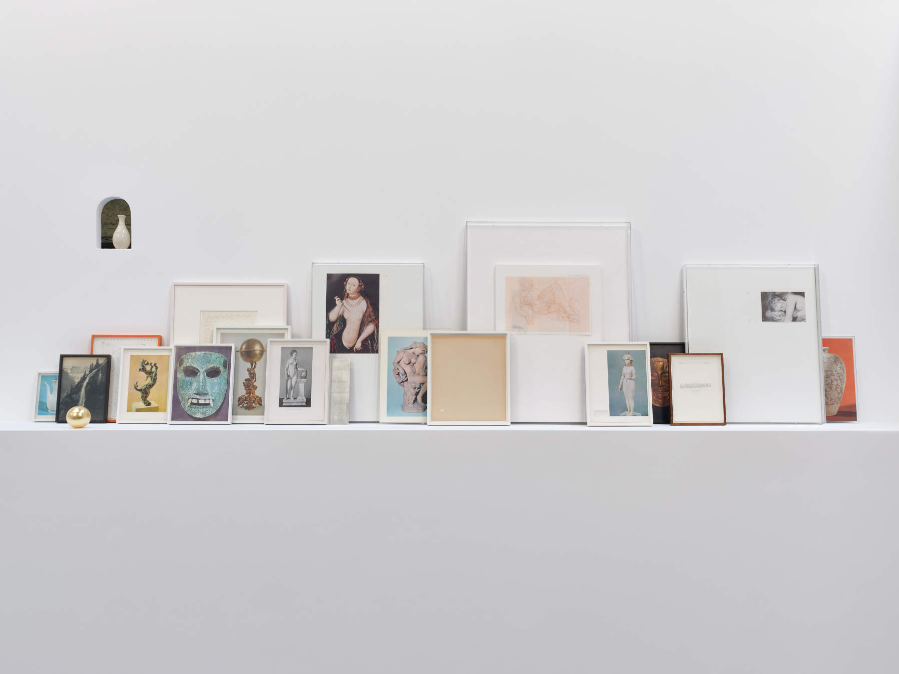 Haris Epaminonda, Untitled #08 c/m (2025; wall with arched window and shelf, small ceramic vase, seventeen recovered pages from books and framed drawings, golden sphere, wooden panel covered in silver leaf with black lacquer, variable dimensions). Courtesy of the artist and Sylvia Kouvali, London / Piraeus. Photo: Stathis Mamalakis