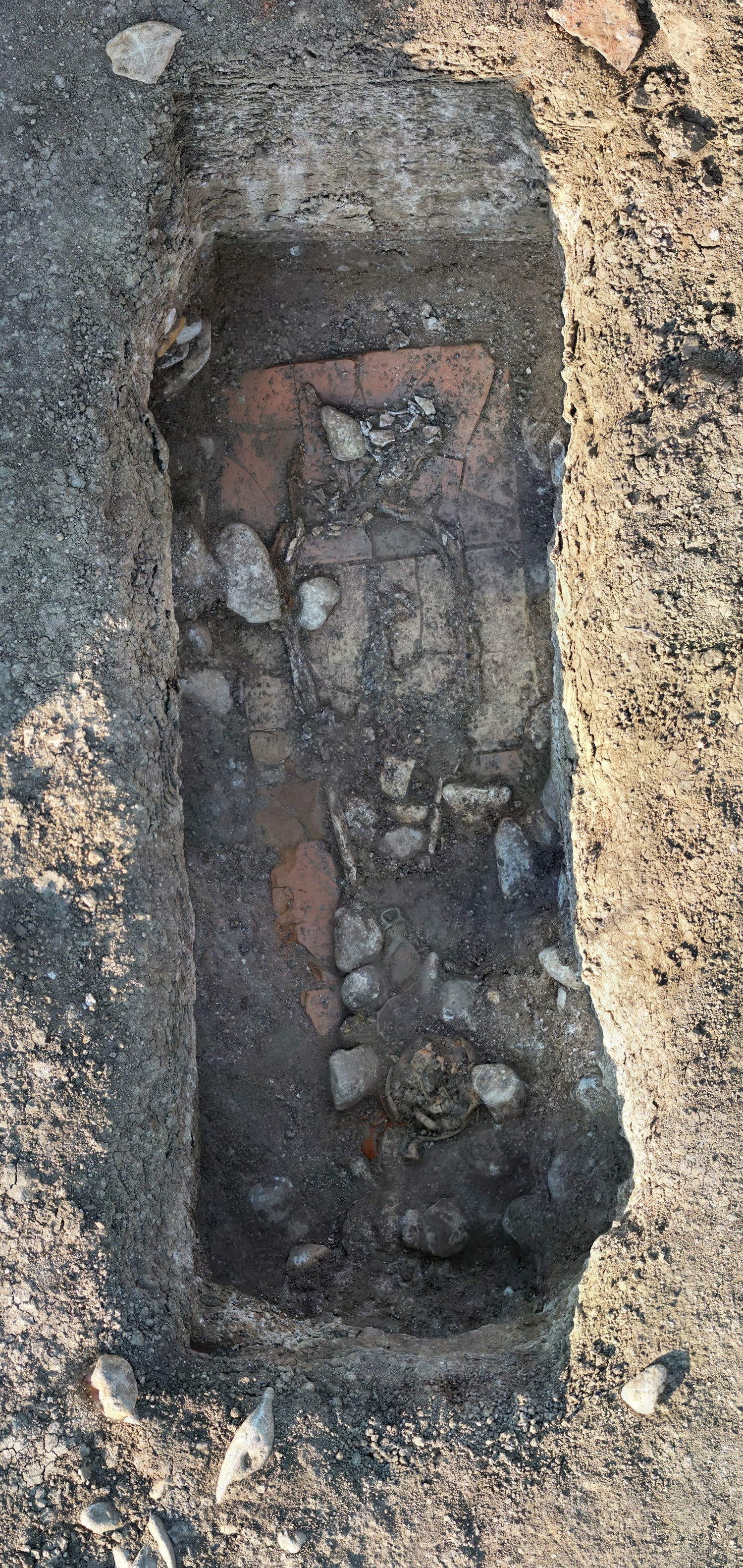 Ejemplo de un enterramiento en curso de excavación con la superficie de deposición en un lecho de baldosas . Se pueden vislumbrar algunos elementos del ajuar funerario y los restos osteológicos del individuo, así como las piedras residuales del relleno de la tumba. Foto: Ministerio de Cultura